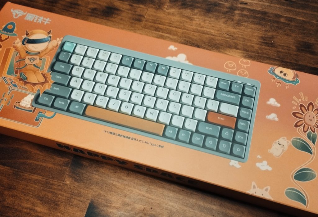 YK75 Tri-Mode Mechanical Keyboardの外装。オレンジ色の地にキーボードの写真とファンシーなキャラクターやイラストレーションが沿えてある。